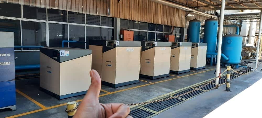Five rotary screw compressors installed in a row at a factory, with vertical air receivers behind