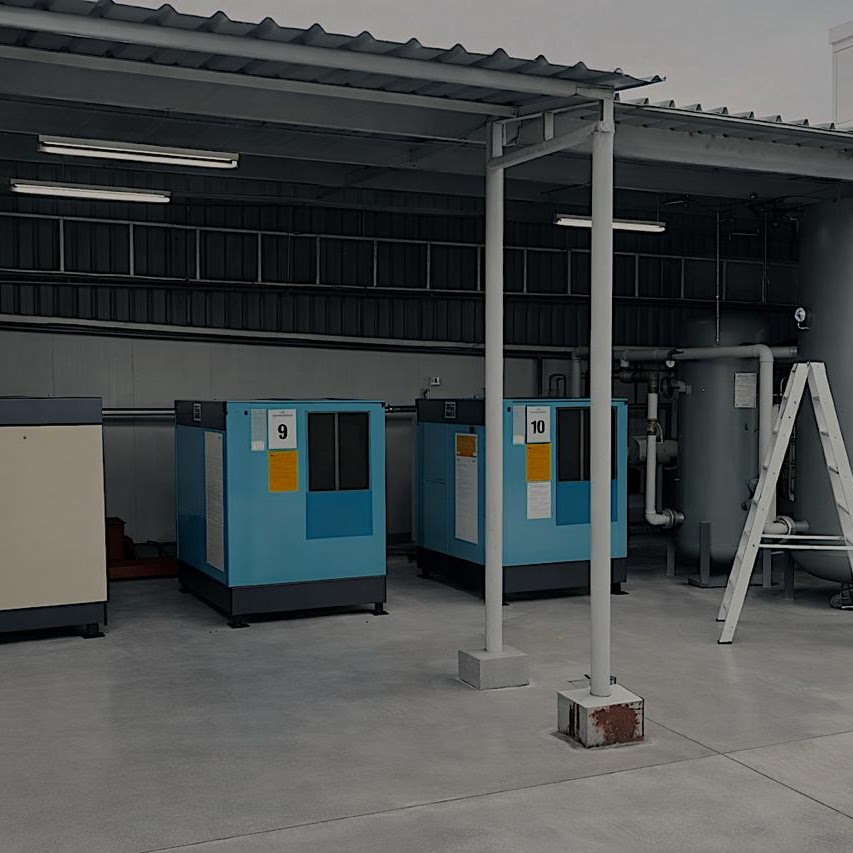 Three air compressors numbered 9 and 10 installed under a covered outdoor compressor house with air receiver