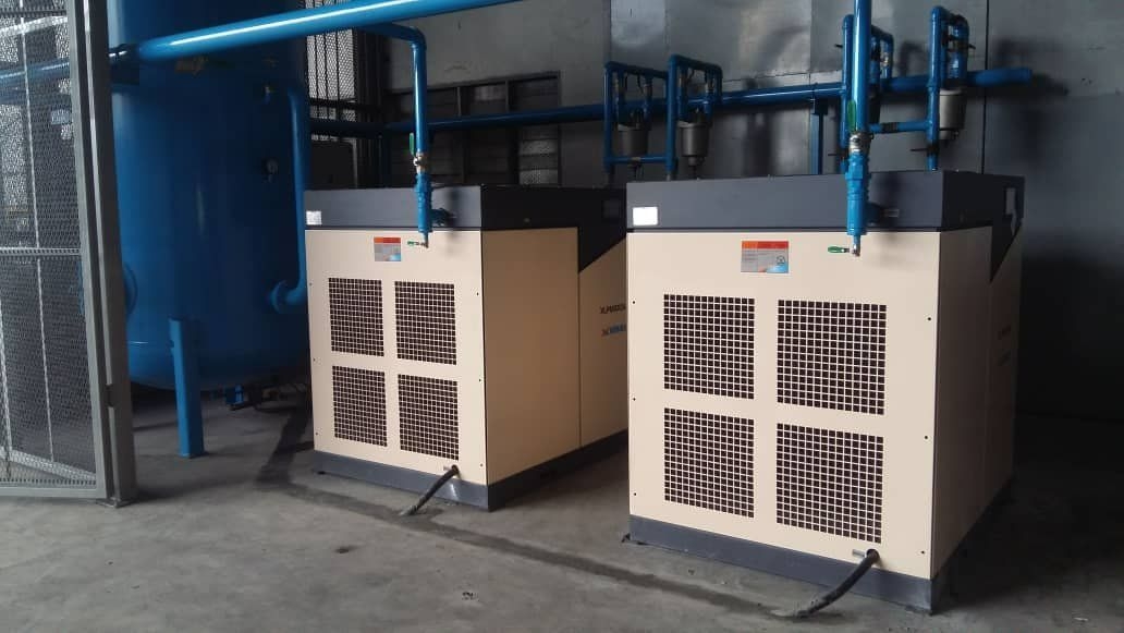 Two rotary screw compressors with refrigerant air dryers and blue compressed air distribution piping in a factory plant room